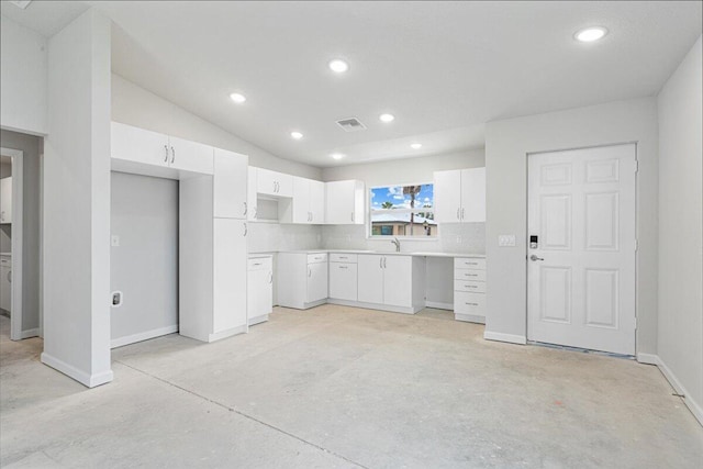 kitchen with concrete flooring, white cabinets, recessed lighting, baseboards, and a sink