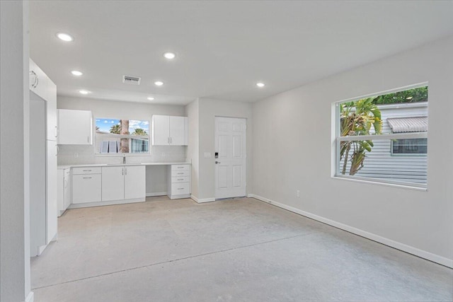 kitchen featuring finished concrete floors, recessed lighting, baseboards, plenty of natural light, and white cabinetry