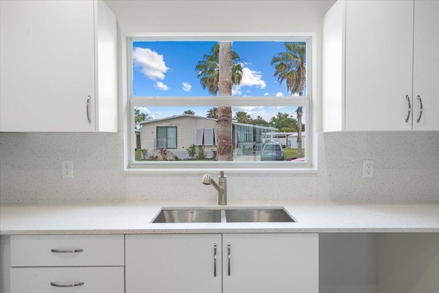 kitchen with a sink, white cabinets, decorative backsplash, and light stone countertops