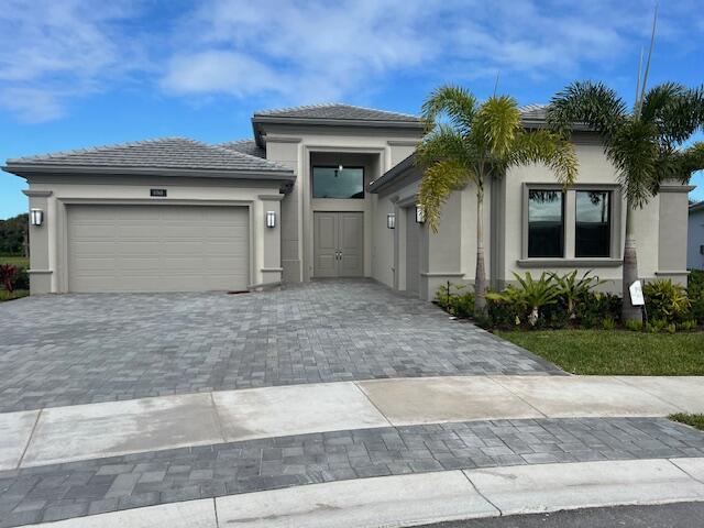 prairie-style home featuring an attached garage, stucco siding, and decorative driveway