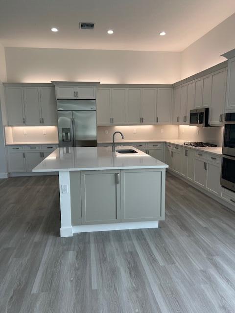 kitchen featuring appliances with stainless steel finishes, a sink, an island with sink, light countertops, and gray cabinetry