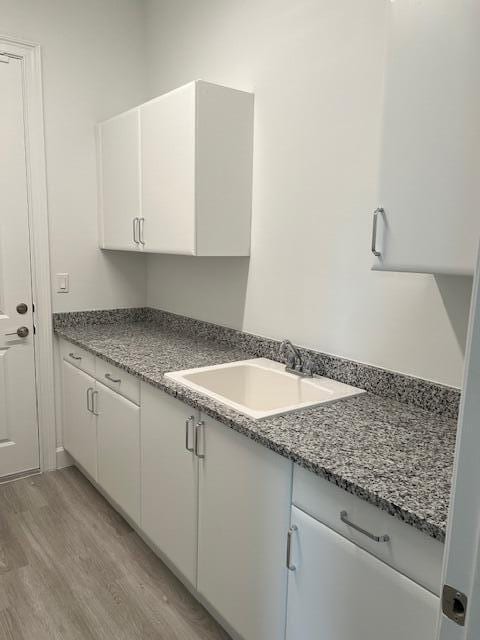 kitchen featuring a sink, light wood-style flooring, white cabinetry, and stone counters
