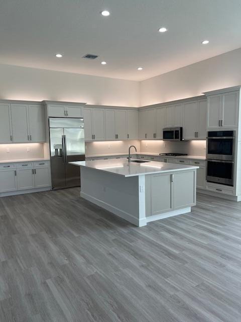 kitchen with stainless steel appliances, a sink, recessed lighting, light wood-style floors, and a kitchen island with sink