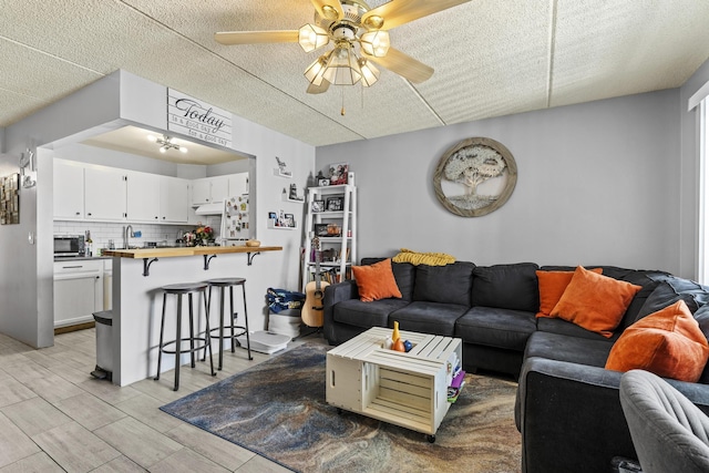 living area featuring a ceiling fan, light wood-style flooring, and a textured ceiling