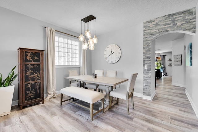 dining room featuring arched walkways, healthy amount of natural light, light wood-type flooring, baseboards, and a textured ceiling