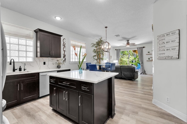 kitchen featuring stainless steel dishwasher, a sink, ceiling fan, open floor plan, and a center island