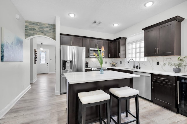 kitchen with stainless steel appliances, arched walkways, a sink, a center island, and a kitchen breakfast bar