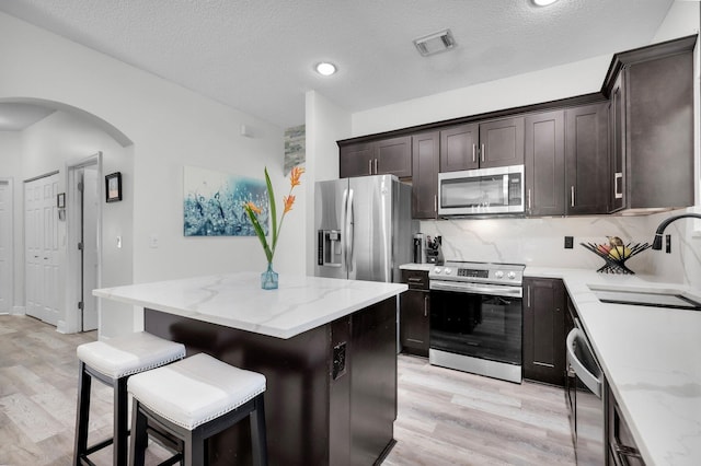 kitchen featuring appliances with stainless steel finishes, a sink, arched walkways, light wood-style flooring, and a textured ceiling