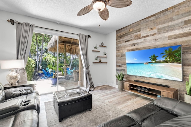 living area with wood walls, a ceiling fan, a textured ceiling, an accent wall, and wood finished floors