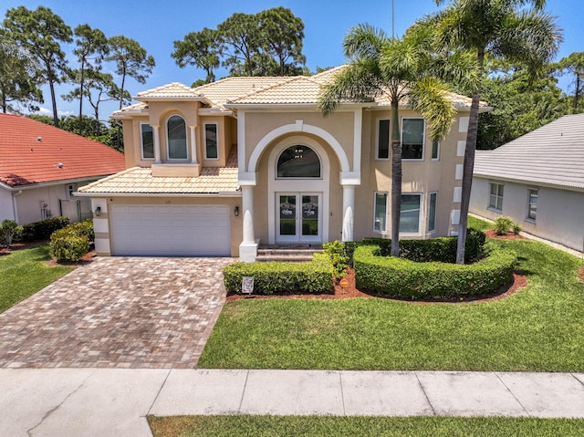 mediterranean / spanish house featuring stucco siding, a tile roof, decorative driveway, a garage, and a front lawn