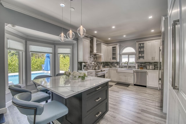 kitchen with stainless steel appliances, ornamental molding, a sink, wall chimney exhaust hood, and tasteful backsplash