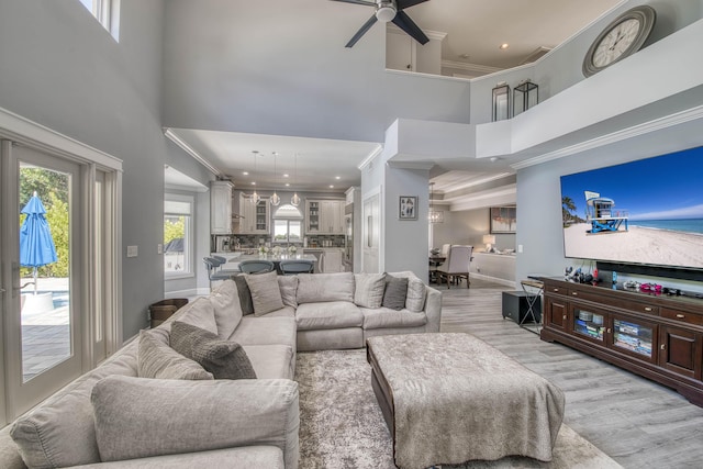 living area featuring a towering ceiling, light wood-style flooring, crown molding, ceiling fan, and recessed lighting