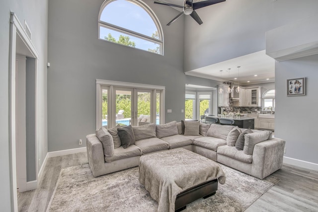 living area with a ceiling fan, a towering ceiling, light wood-style floors, baseboards, and recessed lighting