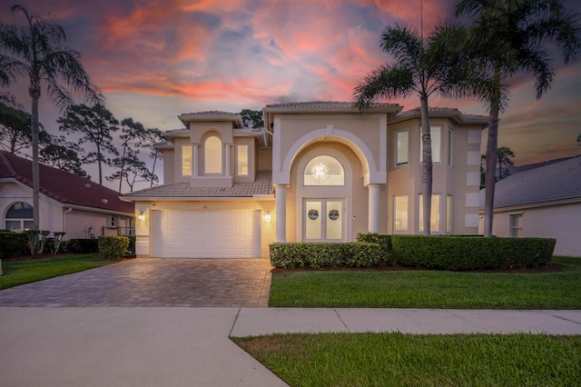 mediterranean / spanish-style home with driveway, stucco siding, a tile roof, an attached garage, and a front lawn