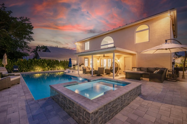 back of house at dusk featuring outdoor lounge area, a ceiling fan, a patio, stucco siding, and a pool with connected hot tub