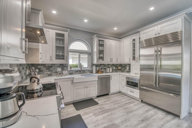 kitchen with appliances with stainless steel finishes, a sink, light stone counters, tasteful backsplash, and light wood finished floors