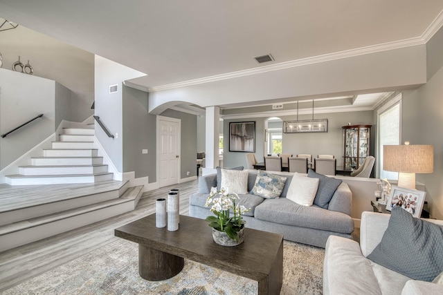 living room featuring arched walkways, wood finished floors, crown molding, stairway, and baseboards