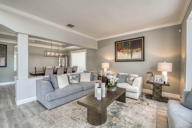 living area featuring wood finished floors, crown molding, baseboards, and a chandelier