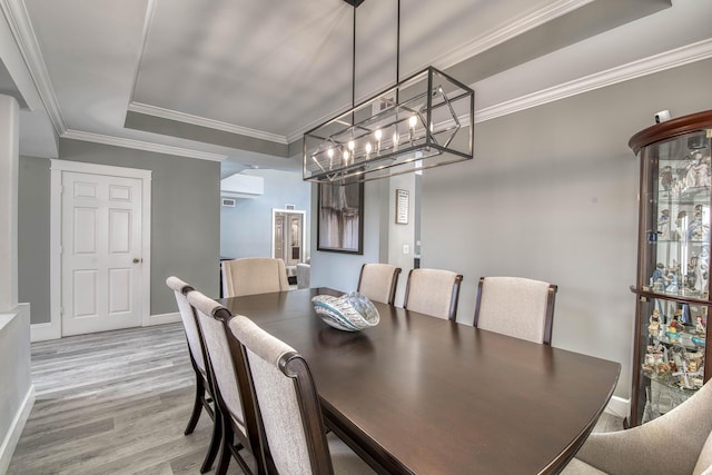 dining room with a tray ceiling, light wood-type flooring, a chandelier, baseboards, and crown molding