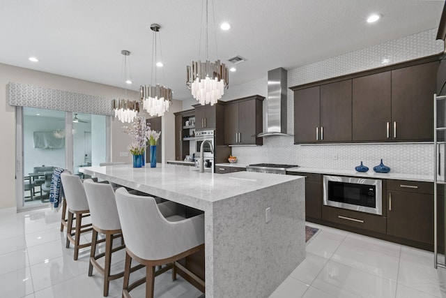 6028 Curie Pl, Palm Beach Gardens, FL 33418 - kitchen with wall chimney range hood, appliances with stainless steel finishes, tasteful backsplash, dark brown cabinetry, and a kitchen breakfast bar
