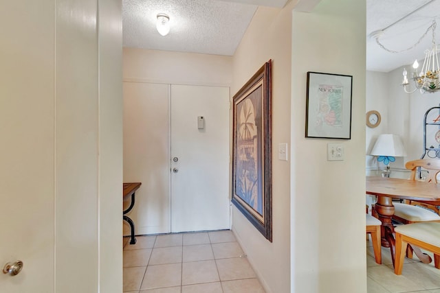 corridor with a textured ceiling, a chandelier, and light tile patterned floors