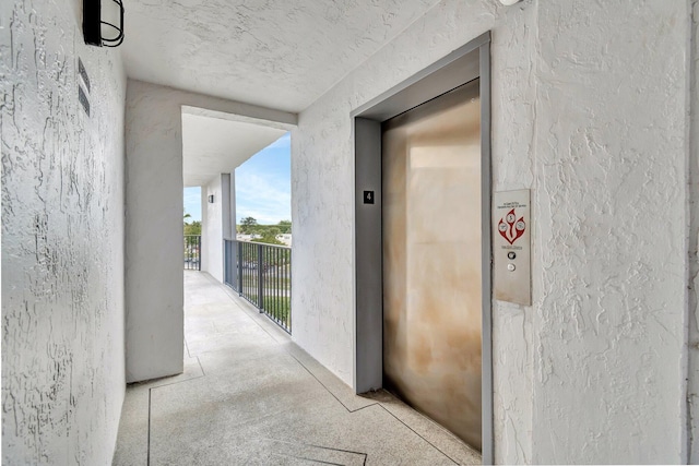 property entrance featuring elevator, a balcony, and stucco siding