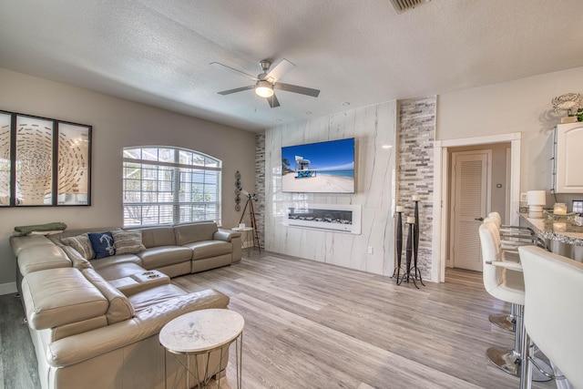 2720 SE Kern Rd, Port Saint Lucie, FL 34984 - living room featuring ceiling fan, light wood finished floors, a textured ceiling, an accent wall, and wood walls
