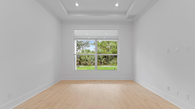 empty room with light wood-style flooring, recessed lighting, a tray ceiling, and baseboards