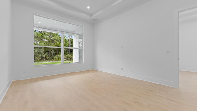 empty room with light wood finished floors, baseboards, recessed lighting, and a raised ceiling