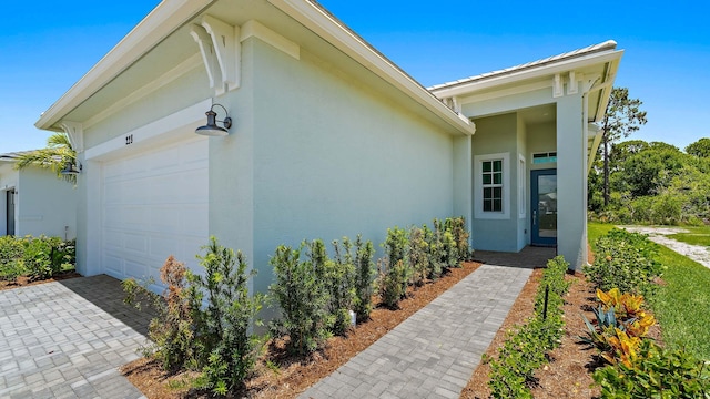 doorway to property featuring an attached garage, stucco siding, and driveway