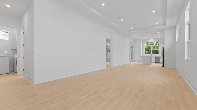 unfurnished living room featuring washer and clothes dryer, light wood-style flooring, recessed lighting, baseboards, and a tray ceiling