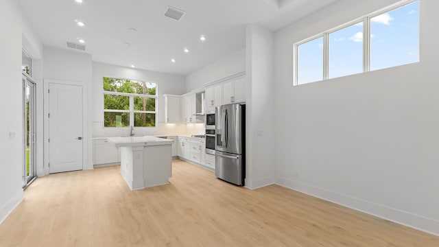 kitchen featuring stainless steel fridge, a center island, light wood-style floors, white cabinetry, and recessed lighting