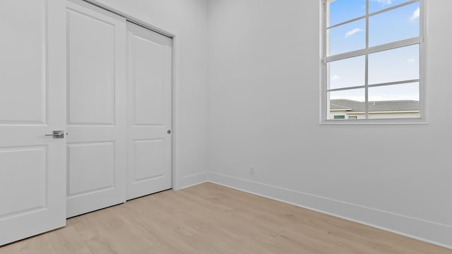 unfurnished bedroom featuring light wood finished floors, baseboards, and a closet