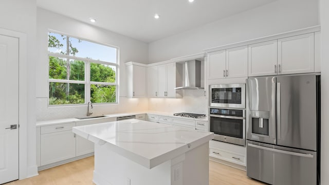 kitchen featuring stainless steel appliances, a sink, wall chimney exhaust hood, light wood-type flooring, and recessed lighting