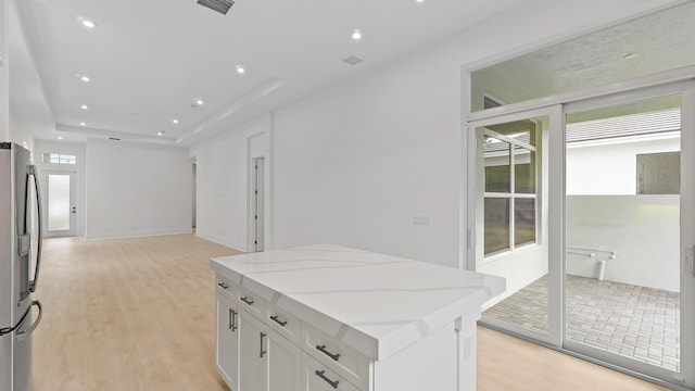 kitchen featuring stainless steel fridge, light wood-type flooring, white cabinets, light stone counters, and open floor plan