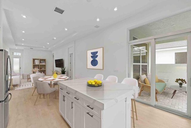 228 SE Via Sangro, Port Saint Lucie, FL 34987 - kitchen with a kitchen breakfast bar, light wood-type flooring, stainless steel refrigerator with ice dispenser, white cabinetry, and a center island