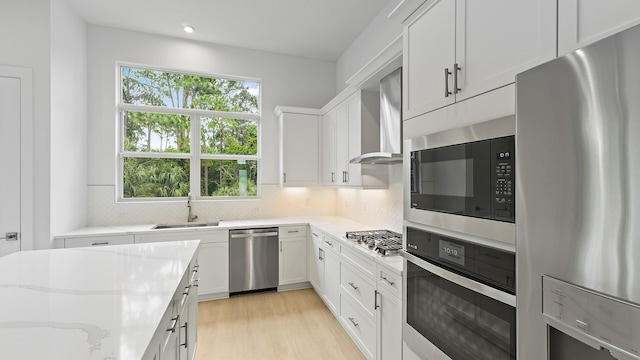 kitchen with appliances with stainless steel finishes, wall chimney range hood, light stone counters, tasteful backsplash, and white cabinetry
