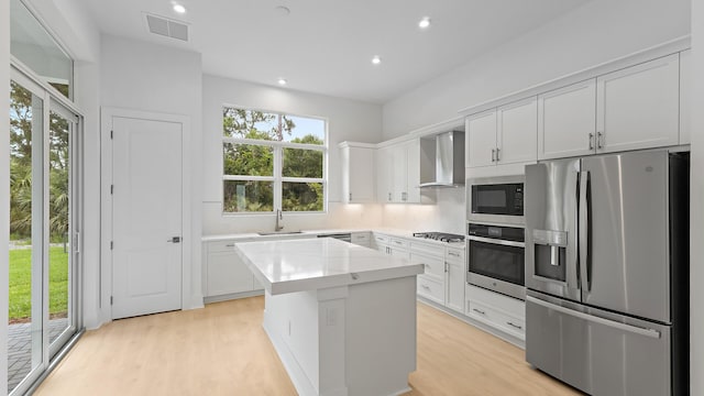 kitchen with stainless steel appliances, wall chimney range hood, a center island, light wood-type flooring, and recessed lighting