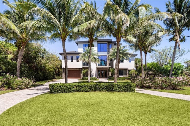 coastal home featuring driveway, stucco siding, a front yard, and an attached garage