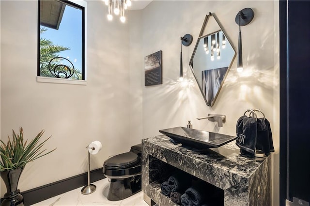 half bathroom featuring toilet, vanity, marble finish flooring, and baseboards