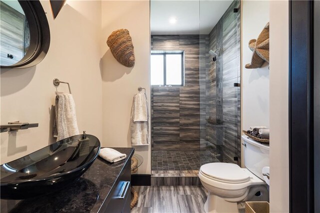 full bath with toilet, a tile shower, vanity, and wood finished floors