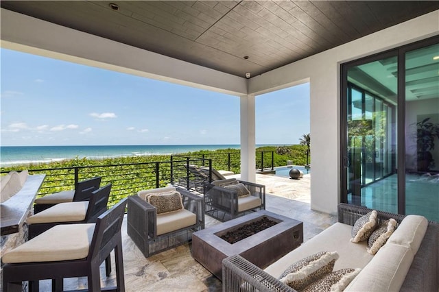 view of patio / terrace featuring an outdoor living space with a fire pit and view of water and beach