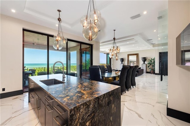 kitchen featuring a sink, a raised ceiling, a chandelier, light marble finish floors, and plenty of natural light
