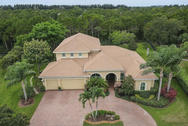 7668 SE Laque Cir, Stuart, FL 34997 - mediterranean / spanish-style house featuring a tile roof, a wooded view, an attached garage, and decorative driveway