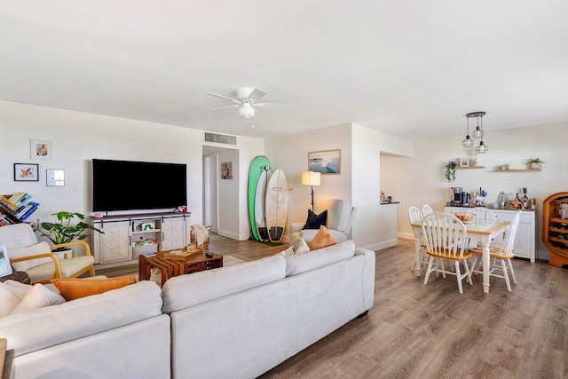 living room with light wood-style flooring, a ceiling fan, and baseboards