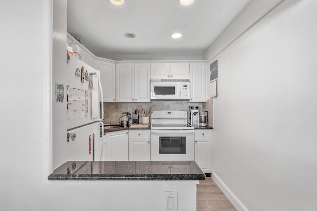 kitchen featuring white appliances, white cabinetry, a peninsula, light wood finished floors, and dark stone counters