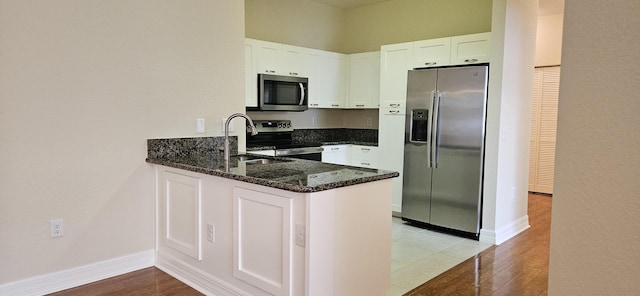 kitchen with stainless steel appliances, dark stone counters, a peninsula, and white cabinetry