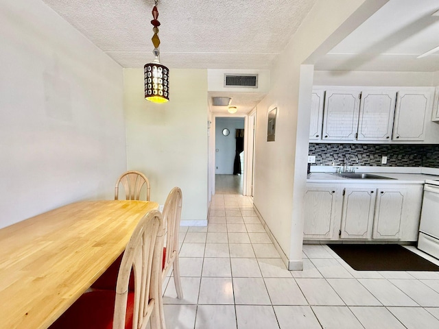 kitchen with a sink, white cabinets, light countertops, light tile patterned floors, and decorative backsplash