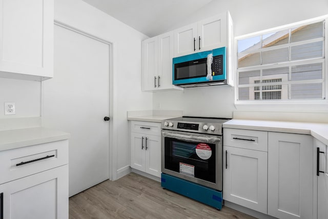 kitchen with electric range, light wood-style flooring, white cabinetry, and light countertops