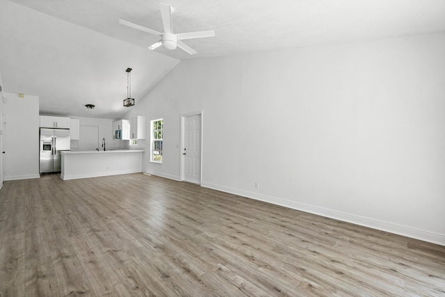 unfurnished living room with wood finished floors, ceiling fan, a sink, baseboards, and high vaulted ceiling